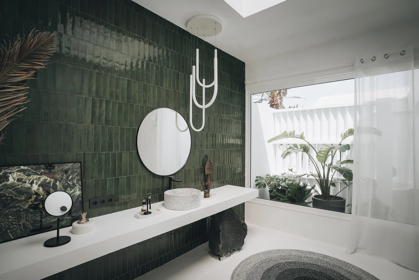 Green tiles, a round mirror and terrazzo basins in the bathroom.