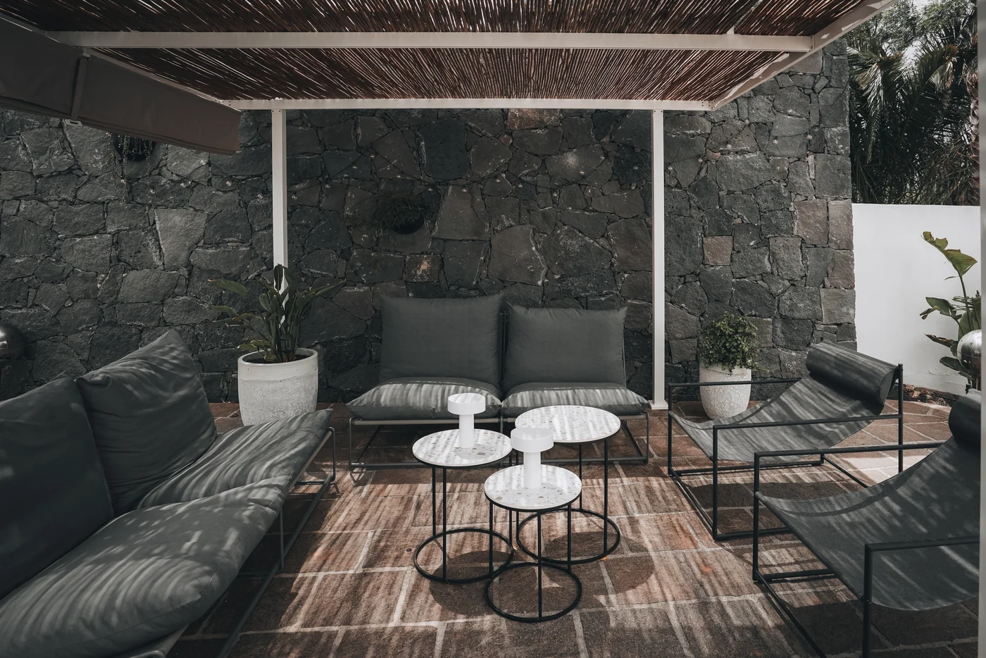 Outdoor sofas beneath the pergola beside a lava-stone wall.